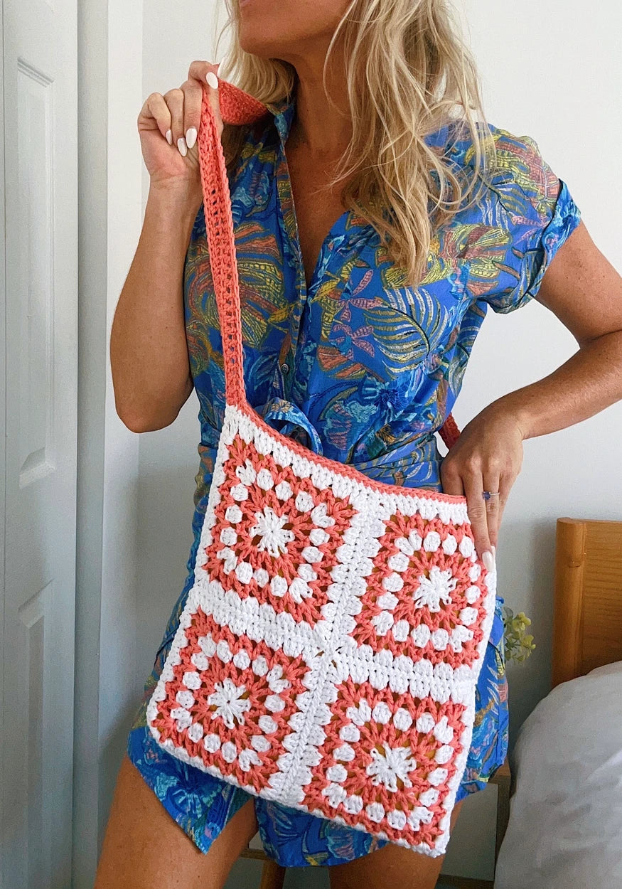 Crochet granny square shoulder bag made with Circulo Aloe Vera yarn in white and coral pink, featuring four large granny squares and a matching crochet strap, styled as a lightweight handmade summer accessory.