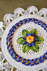 Circulo Barroco Multicolor Premium 4/6 - Brazilian Cotton Yarn, 226m/200g - A round crocheted doily with a white base, featuring a central green and blue flower motif with a yellow-orange center, surrounded by blue and yellow floral borders.