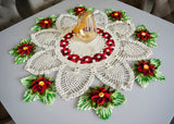 Circulo Barroco Natural Brilho  - Natural Cotton Yarn Gold/Silver, 657m / 433m, 400g - A crocheted holiday table runner or doily set on a gray table, featuring white lace petals with red and green poinsettia flowers and a central red-and-black pattern, with a small glass bottle placed on top.