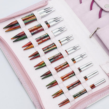 KnitPro Symfonie 2 Special interchangeable needle set, 10 cm, Deluxe - A pink fabric needle case holding multiple knitting needles arranged in elastic loops. The needles have silver metal tips and colored shafts in green, orange, red, and brown tones, with some white text printed on them.